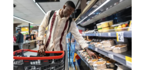 Shopper selecting a prepared grab-and-go meal from a refrigerated grocery case.