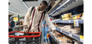 Shopper selecting a prepared grab-and-go meal from a refrigerated grocery case.